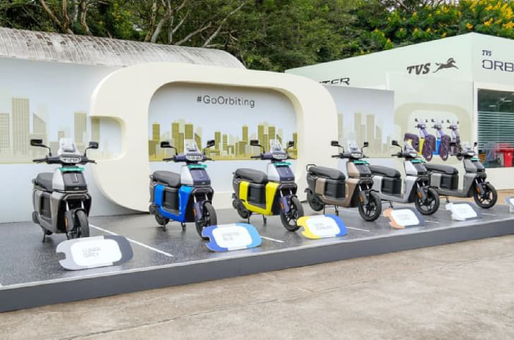 Six TVS Orbiter scooters in different colors on a stage